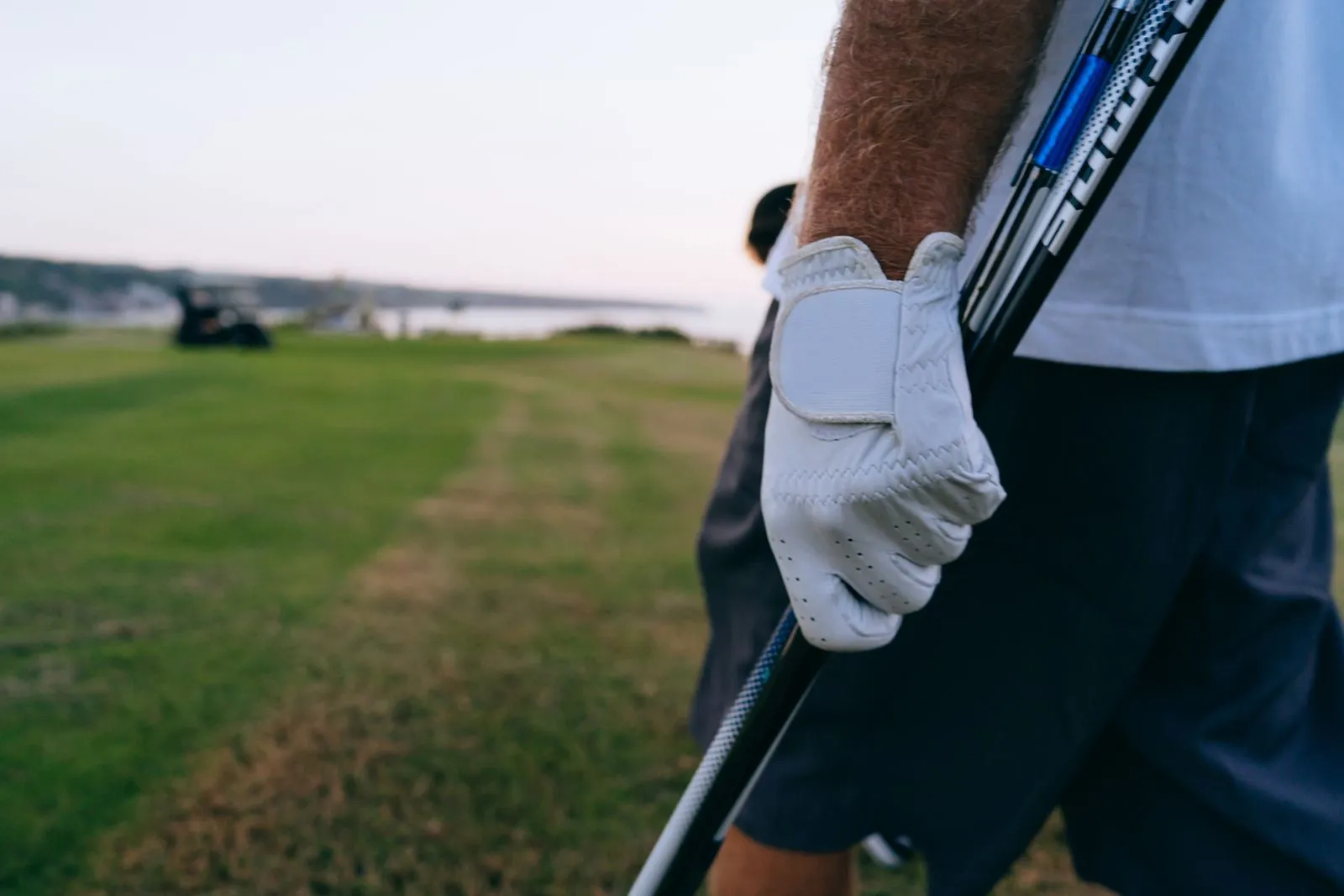 Close-up of a golfer's gloved hand holding a club on a beautiful golf course.